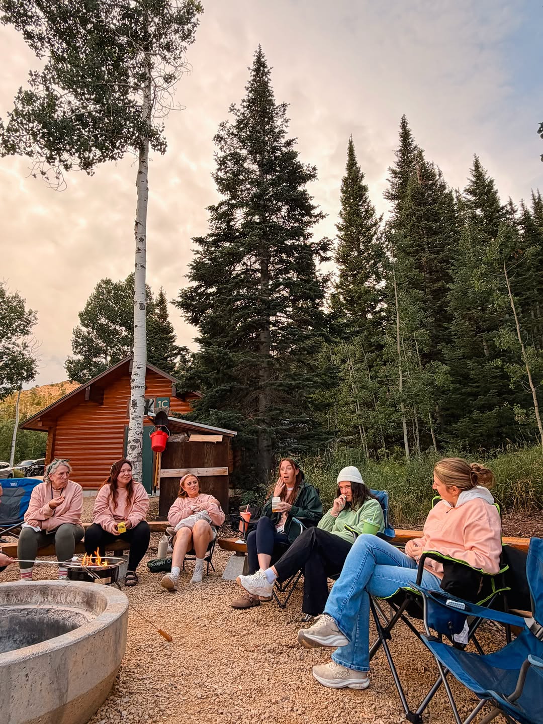 Campers relaxing and chatting around a campfire beside a cabin