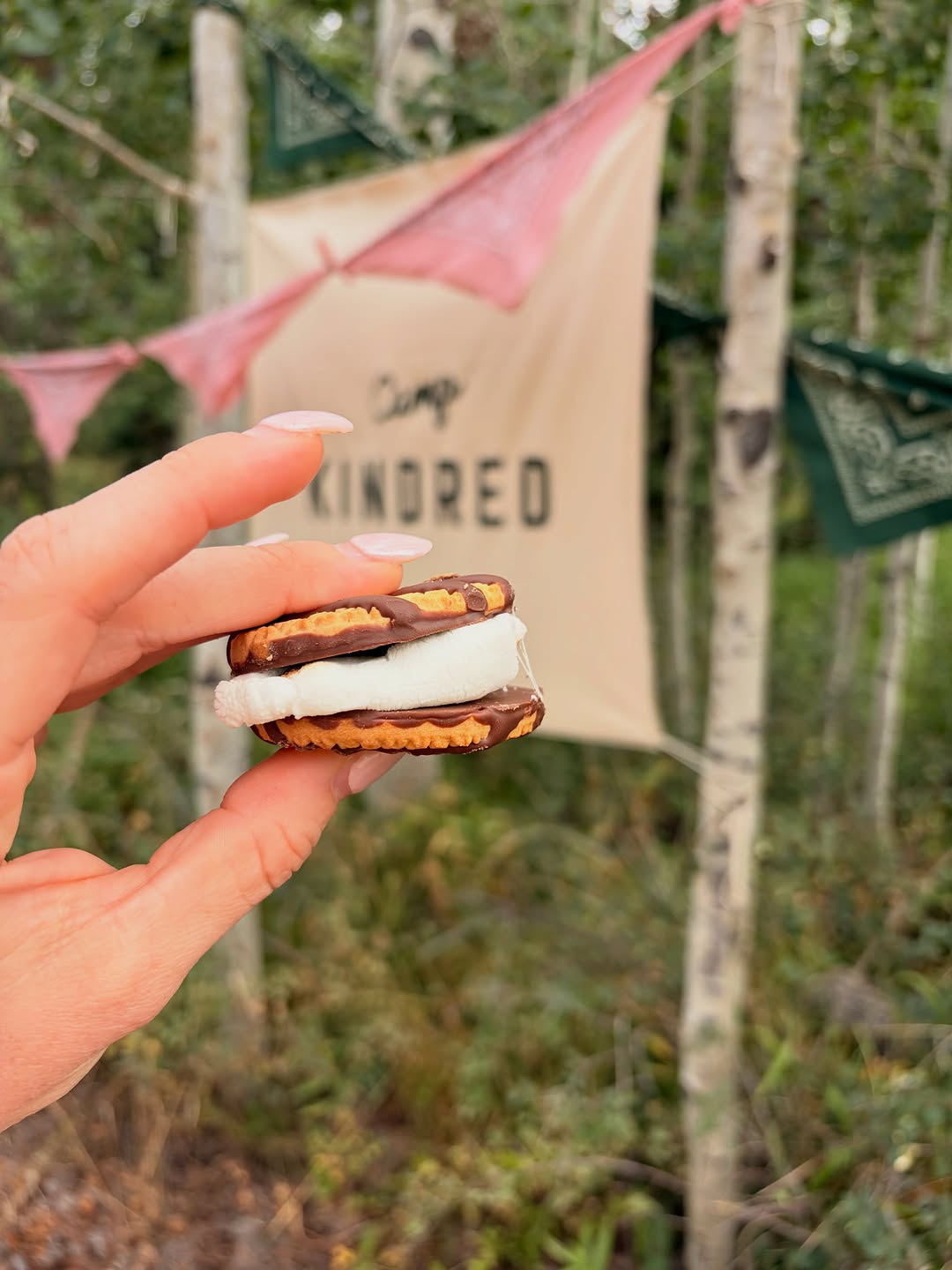 A s’more held in front of the Camp Kindred banner